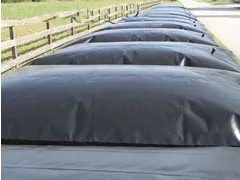 Row of black water storage bladder tanks aligned along a wooden fence, used for agricultural or industrial purposes.